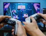 Dwie osoby grają w grę na konsoli PlayStation 5, trzymając kontrolery DualSense.