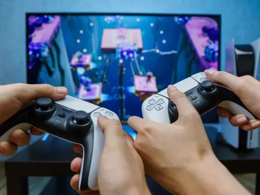 Dwie osoby grają w grę na konsoli PlayStation 5, trzymając kontrolery DualSense.